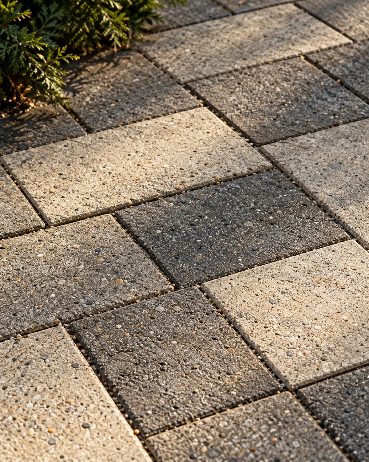 Close view of limestone-gray and charcoal textured concrete pavers in low side light, showing narrow sand-filled joints